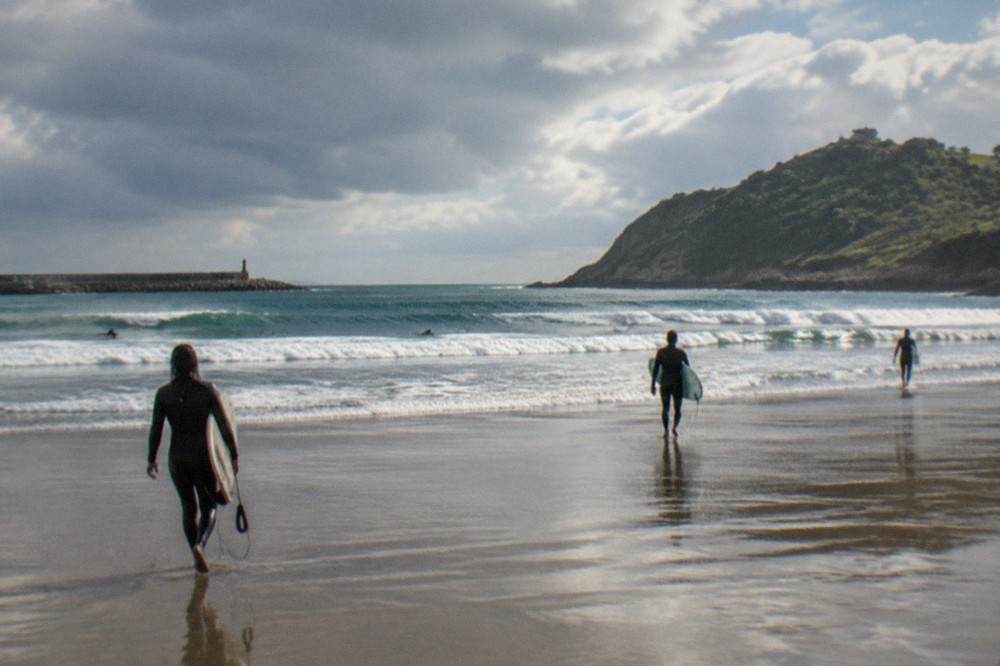 Surfers carrying boards walking across wet sand toward breaking waves