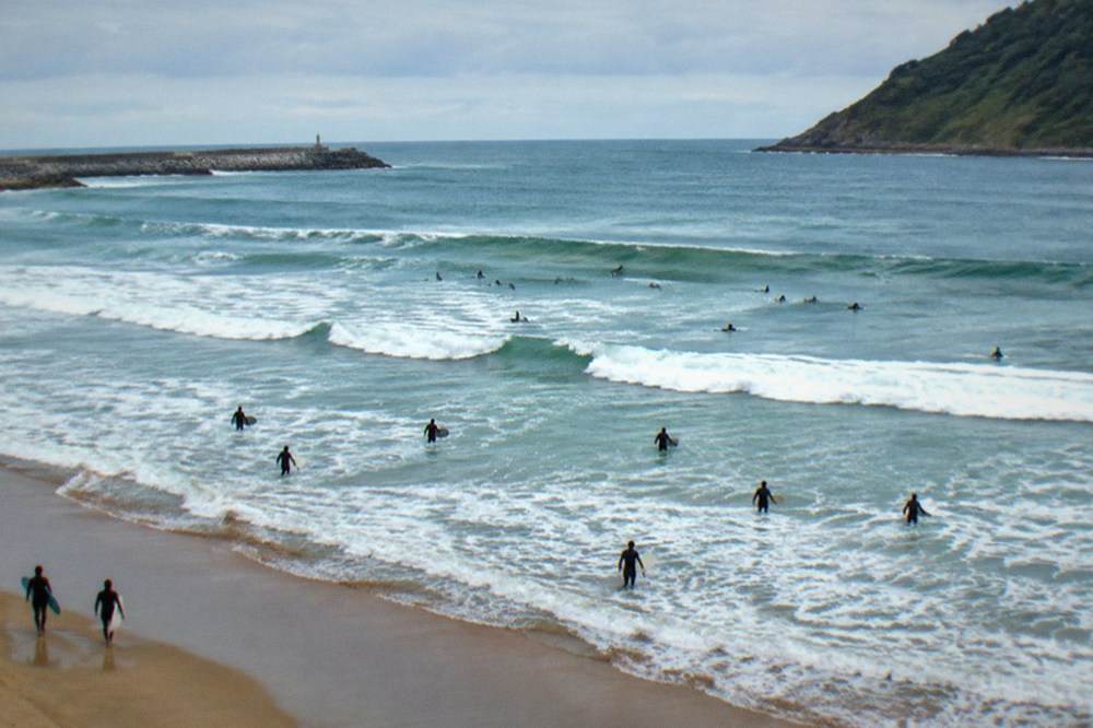People in wetsuits paddling out through whitewater at a city beach