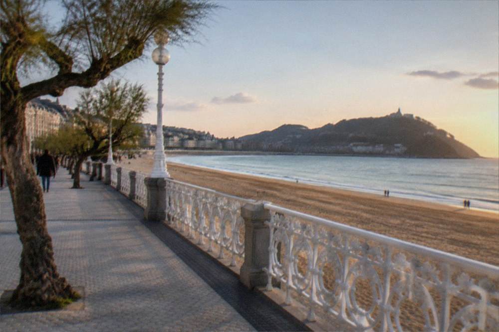 Evening light on a sandy beach with a promenade and distant headland