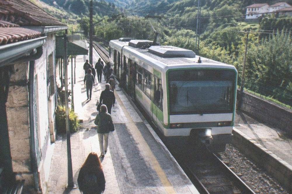 A single-car narrow-gauge train at a small Basque station platform, green hills behind the track