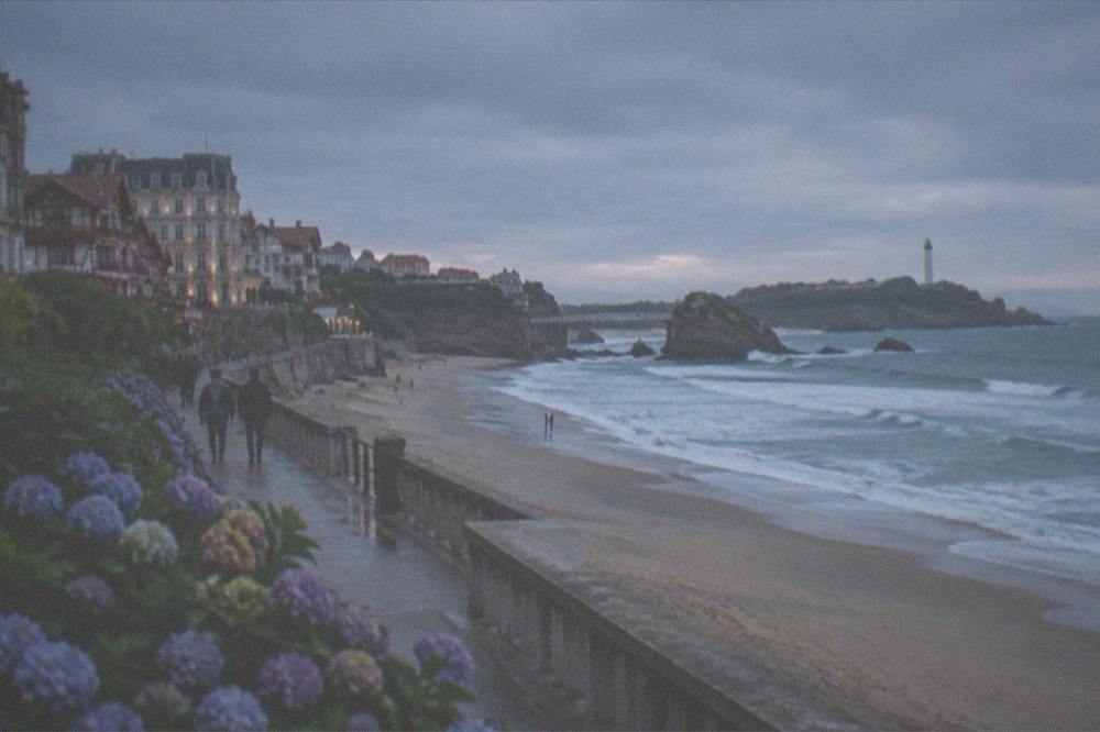 A long Atlantic beach under a grey sky, a boardwalk running along the sand toward distant cliffs