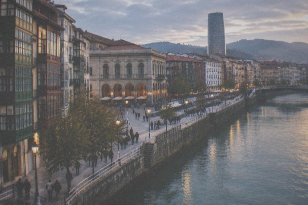 Evening light on the riverfront buildings of Bilbao with people walking along the bank