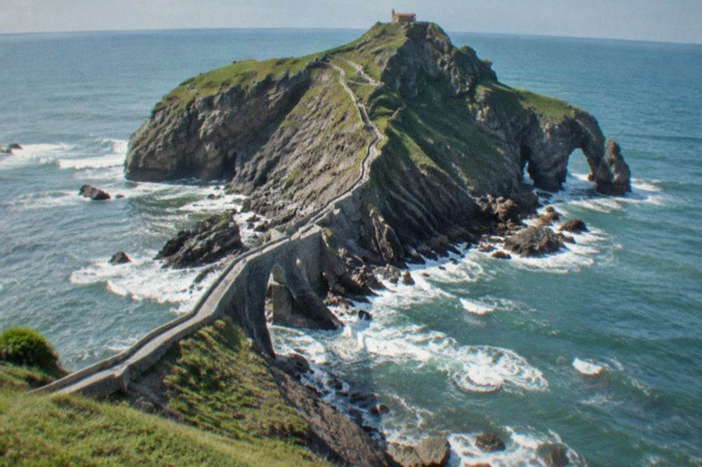 The narrow stone footbridge crossing from the mainland to the rocky islet, with waves breaking below