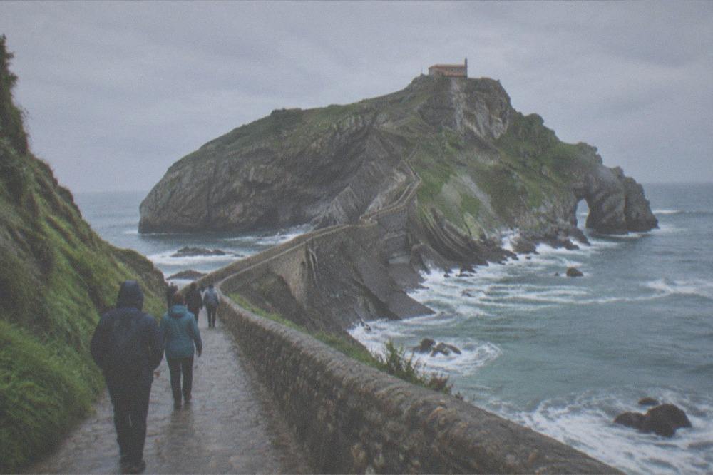 A small group of visitors walking the coastal path towards the islet, wearing windbreakers