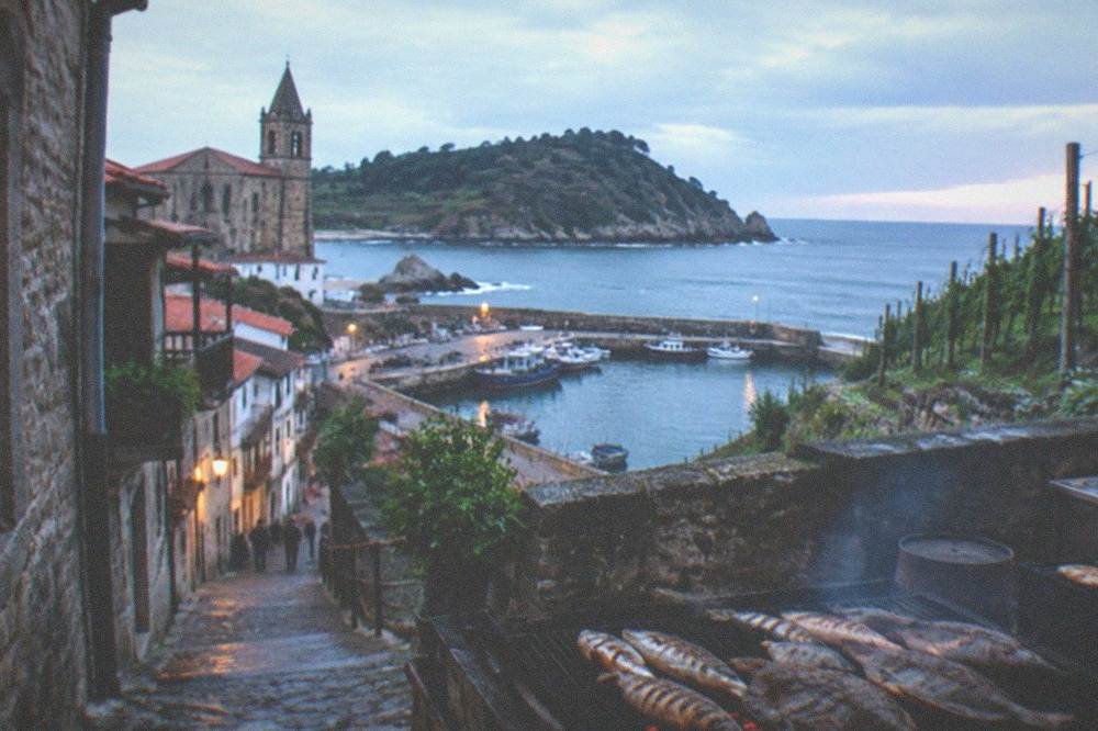 A narrow old street with stone buildings leading down toward a small harbour