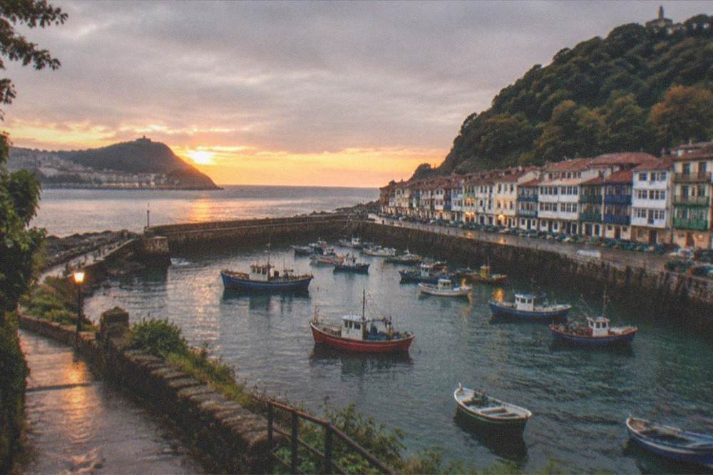 A view from a hillside path over a small coastal town with boats in the harbour at sunset
