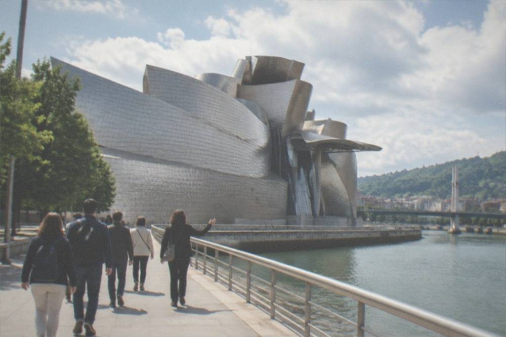 A small group of visitors following a guide along the riverside path beside the Guggenheim Museum