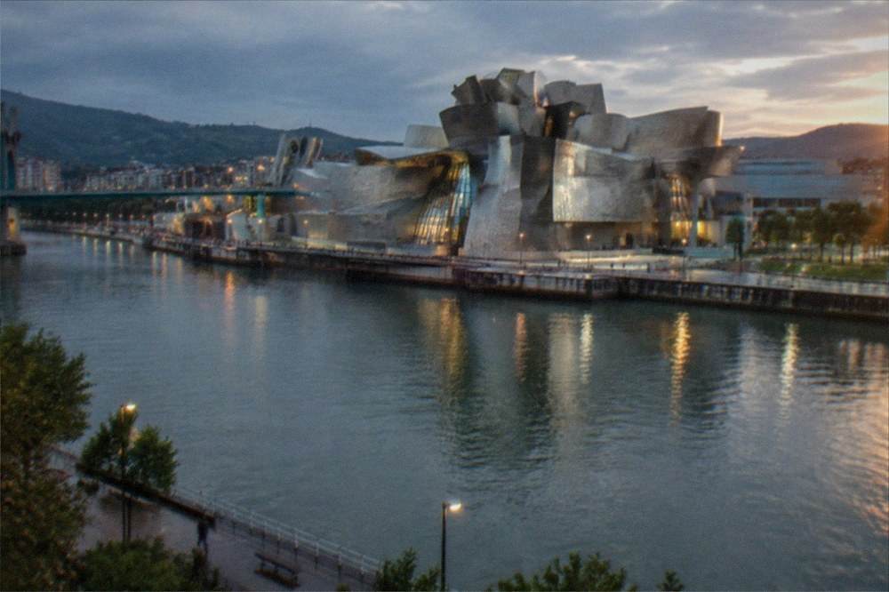 The Guggenheim Museum seen from across the river at dusk with the city lights reflecting on the water