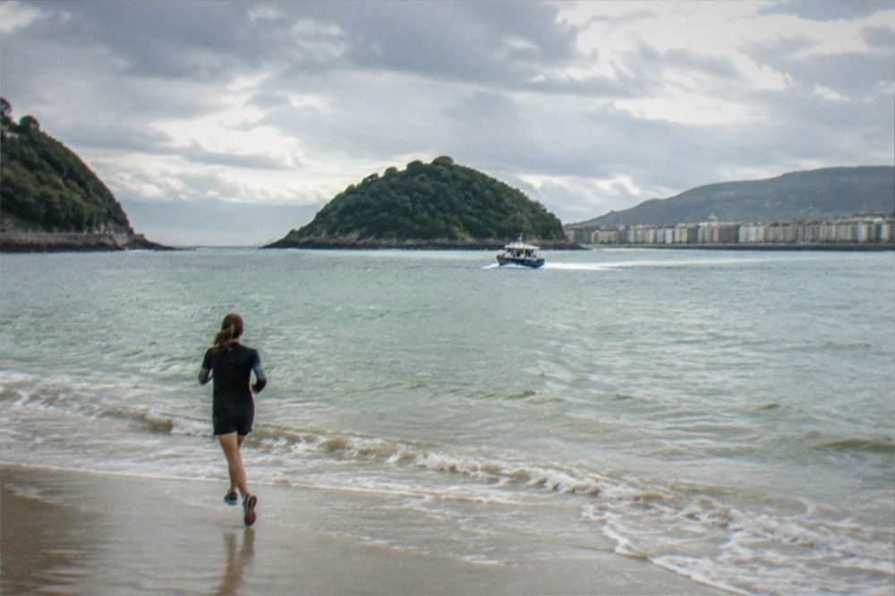 A small boat crossing La Concha bay toward a green island