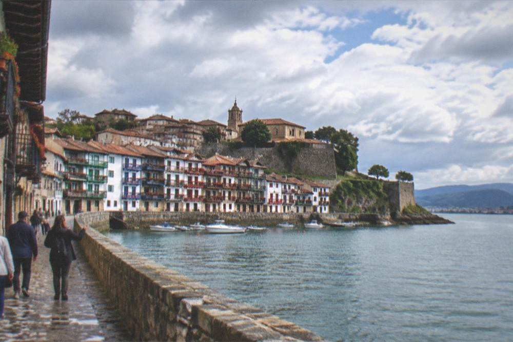A small group of visitors walking with a guide along the harbour wall in Hondarribia