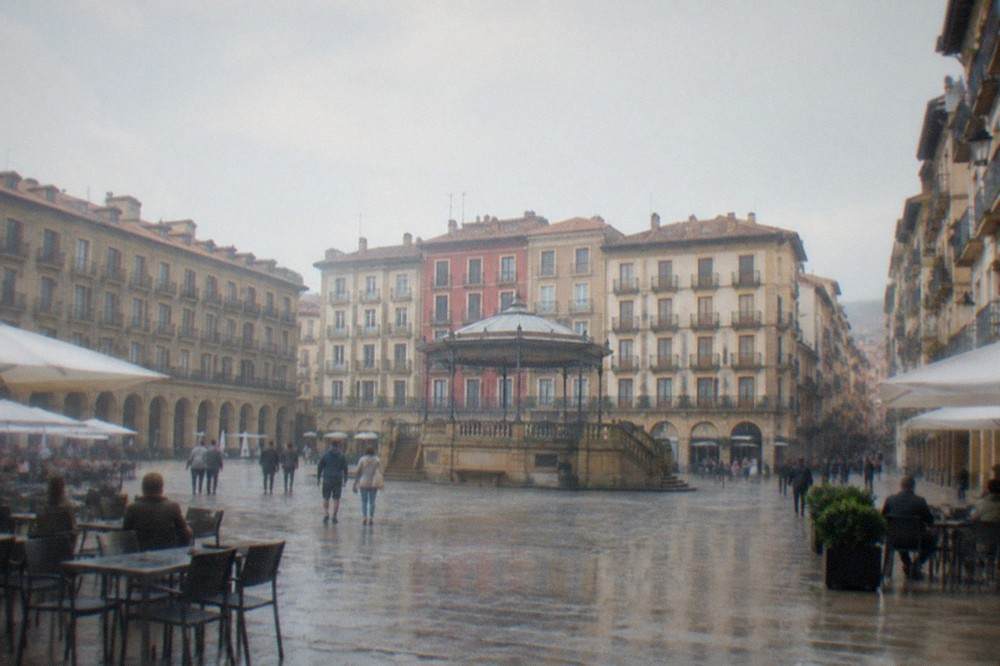 A stone-paved square in Pamplona's old town with cafe tables and balconied buildings