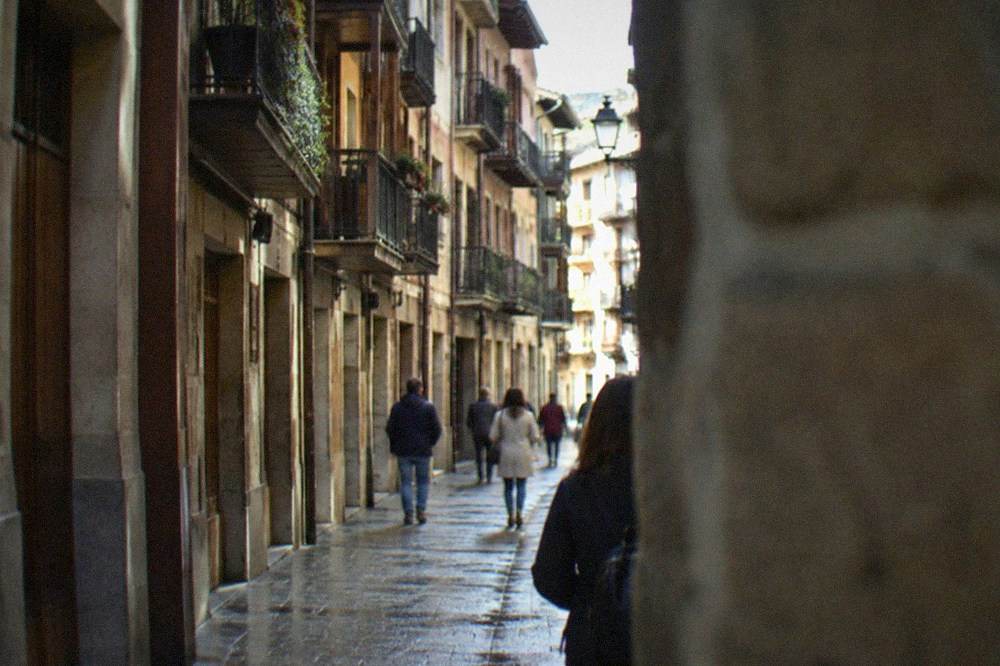 A narrow old street in Pamplona with wooden balconies above and stone paving below