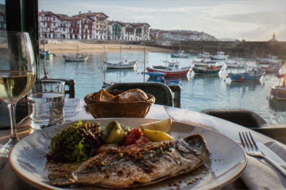 A plate of grilled fish with a red Espelette pepper garnish on a restaurant table