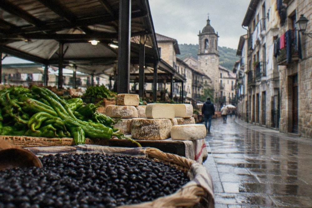 A narrow street of stone buildings with hanging laundry and a church tower in a Basque town