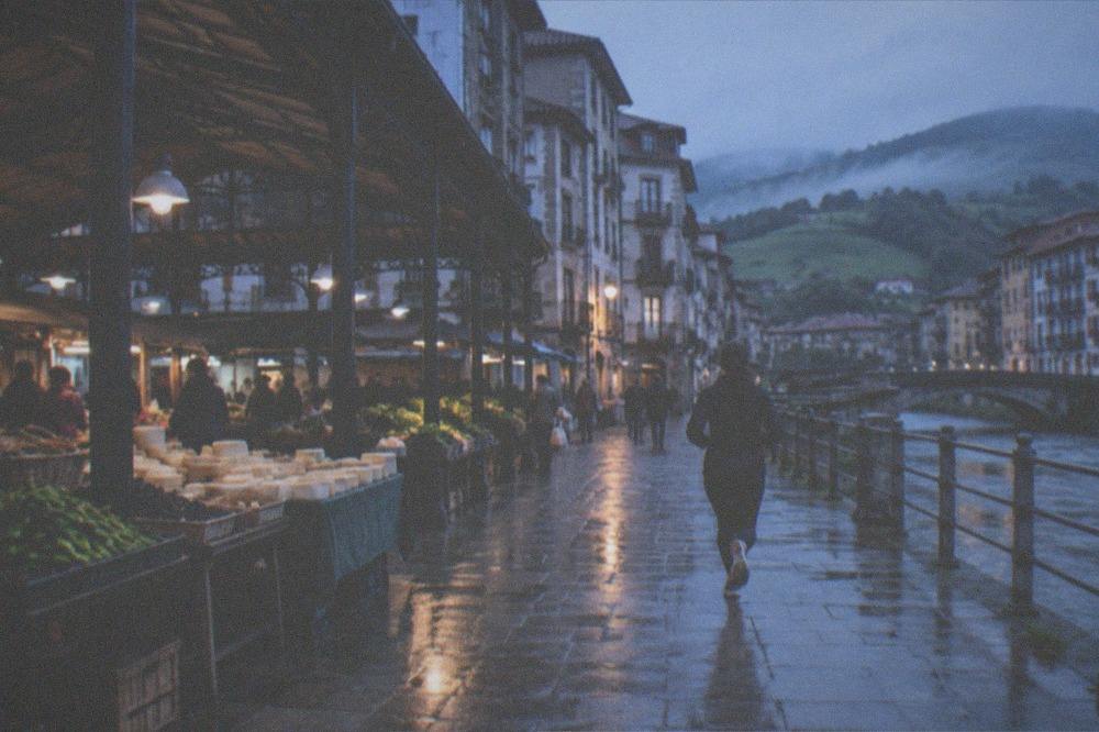 A winding road through green hills with farmhouses and mist in a Basque valley