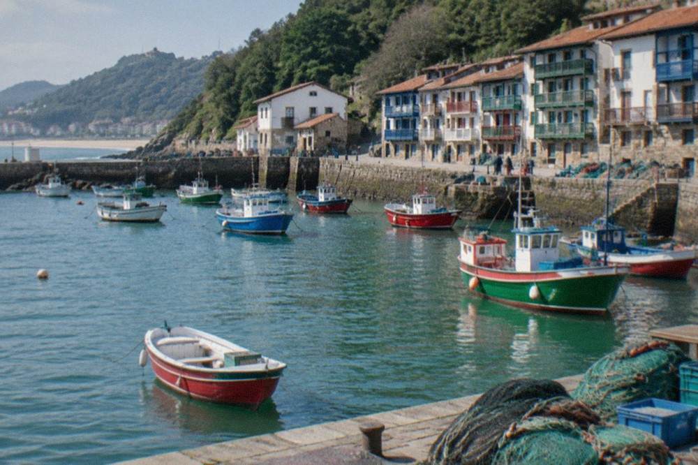 A stone breakwater and small fishing boats at the west end of a Basque beach town