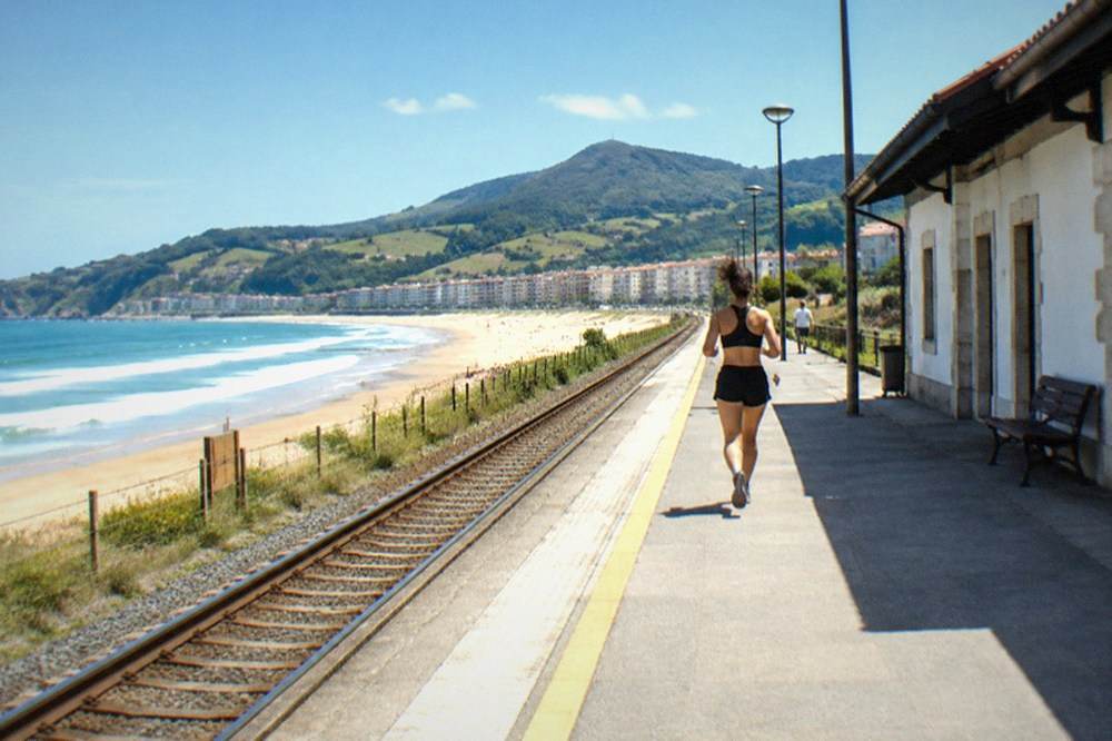 A single-track railway platform beside a low station building in a Basque coastal town