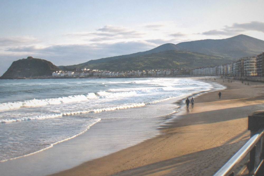 A small Basque fishing port with white houses and a rocky peninsula beyond