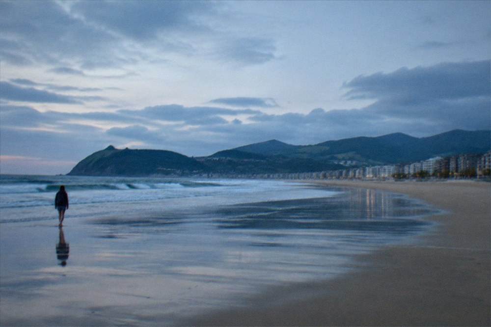 Empty wet sand on a long beach in soft evening light with clouds over the sea