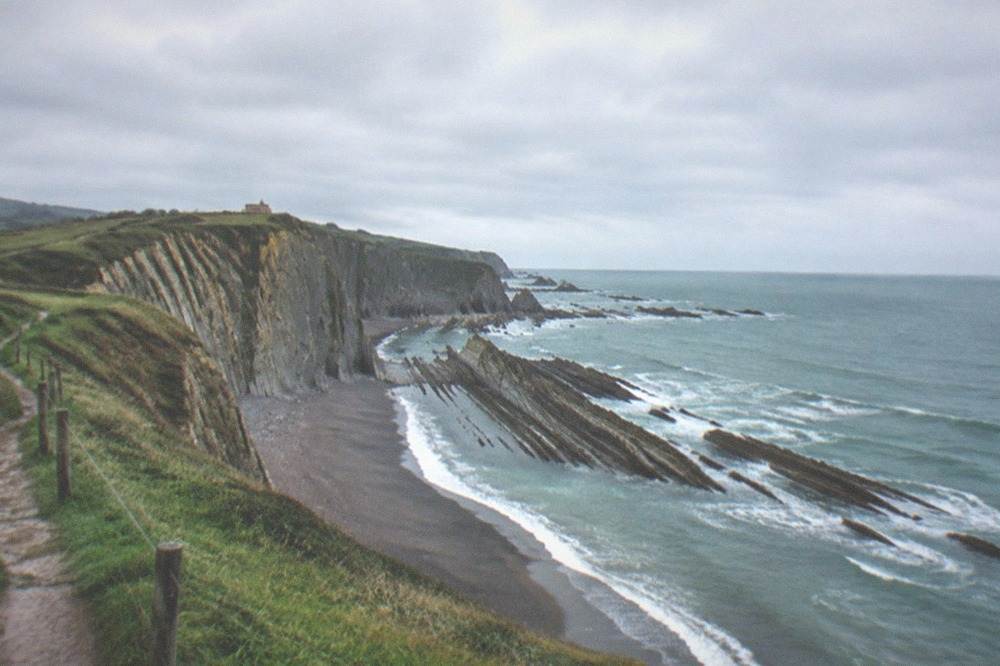 A grassy clifftop path above layered cliffs on the Basque coast
