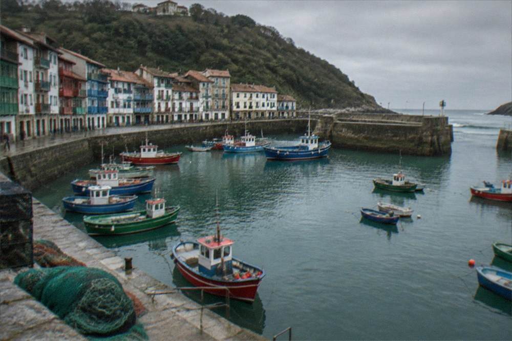 Fishing boats in a small Basque harbour town below green hills