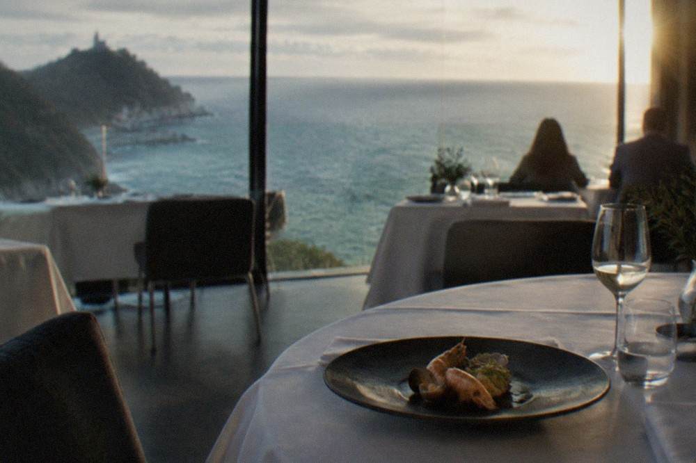 A plated seafood course with shellfish arranged on a dark ceramic dish