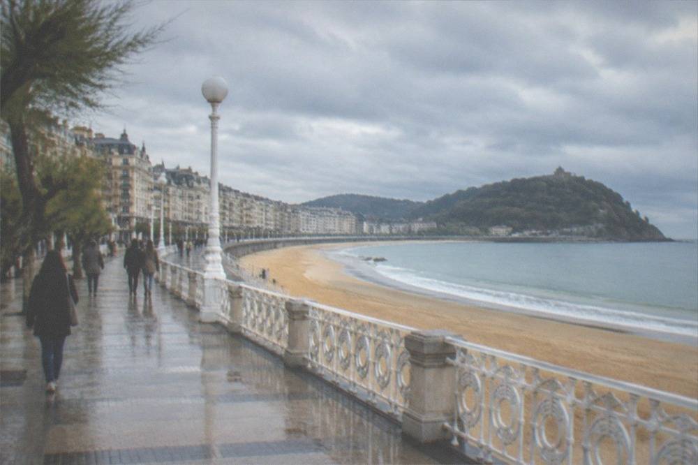 People walking along a curved bay promenade under a cloudy sky