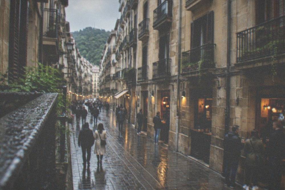 Rain-washed balcony railing above a wet Old Town street with lit bar windows