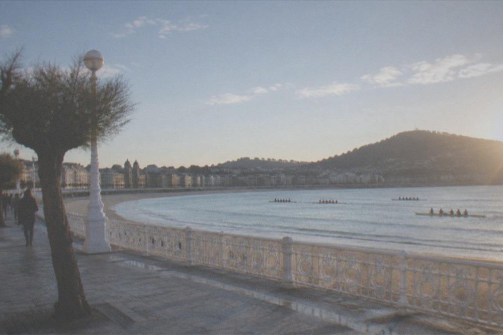 Rowing boats racing across a calm bay in front of a city promenade