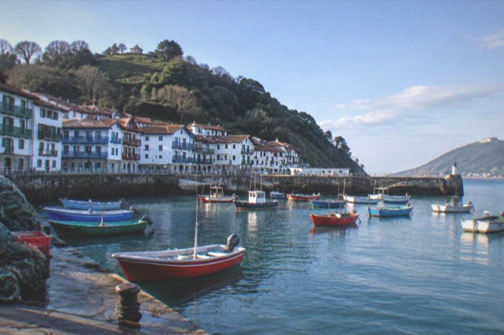 A small fishing boat harbour with white houses and green hills behind