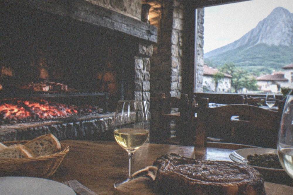 A table set with grilled meat, bread and glasses of white wine in a rustic dining room