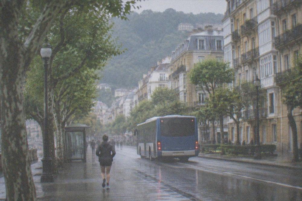 A city bus pulling away from a stop on a tree-lined street in San Sebastián