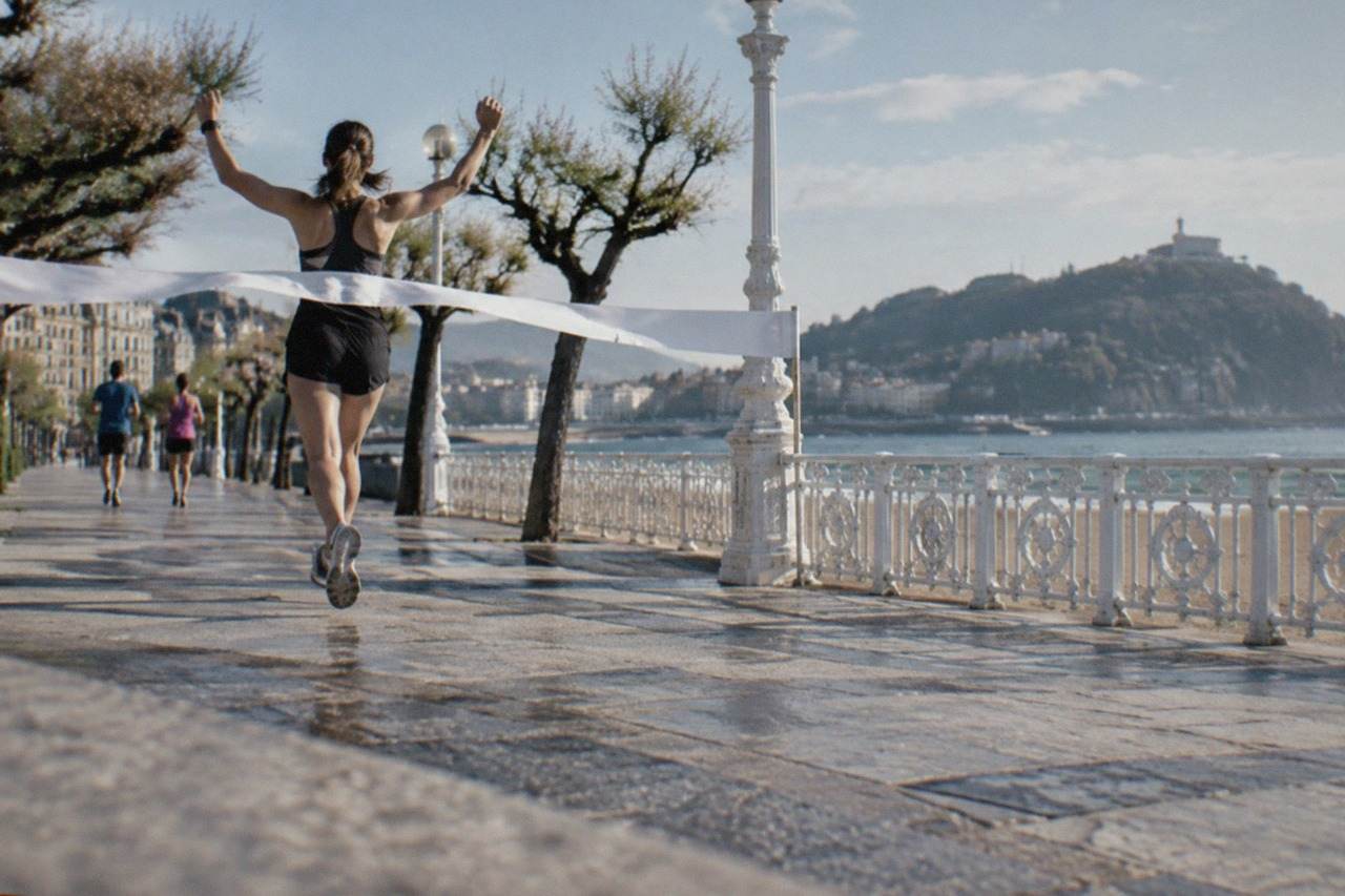 Runners crossing a finish line on a seafront promenade beside a wide bay