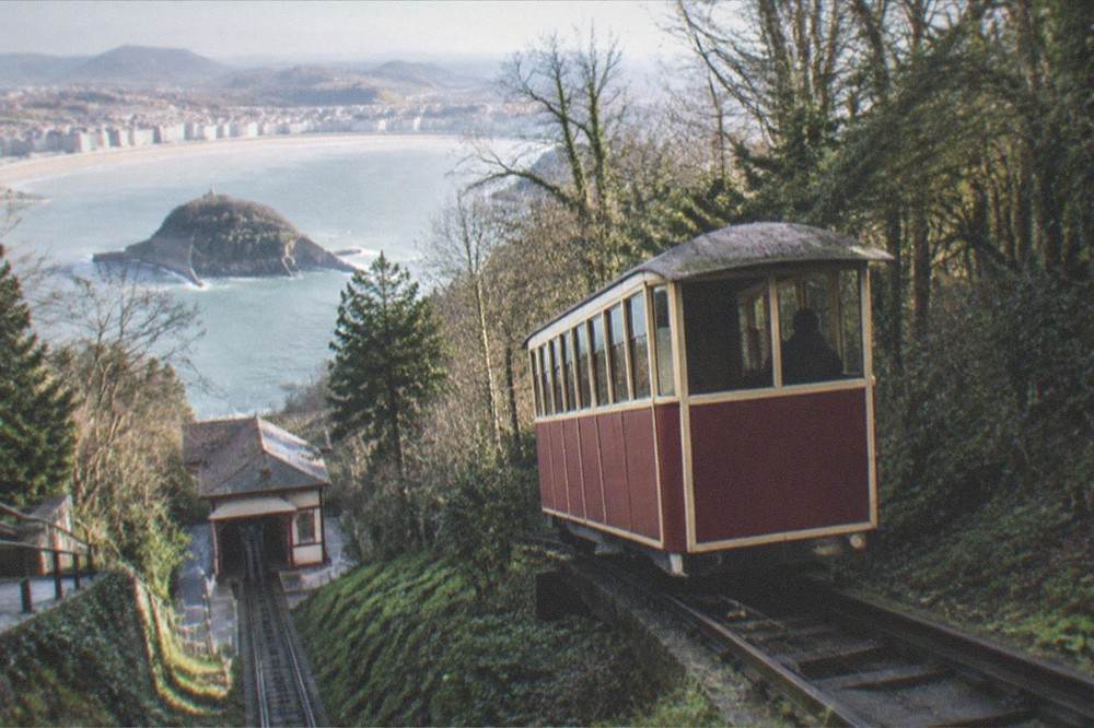 A wooden funicular car climbing a wooded hill above a bay