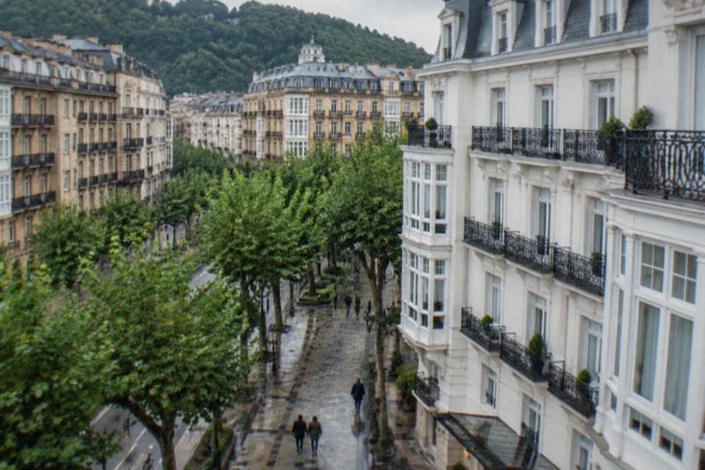 A grand white hotel facade with wrought iron balconies beside a tree-lined street in the centre of San Sebastián