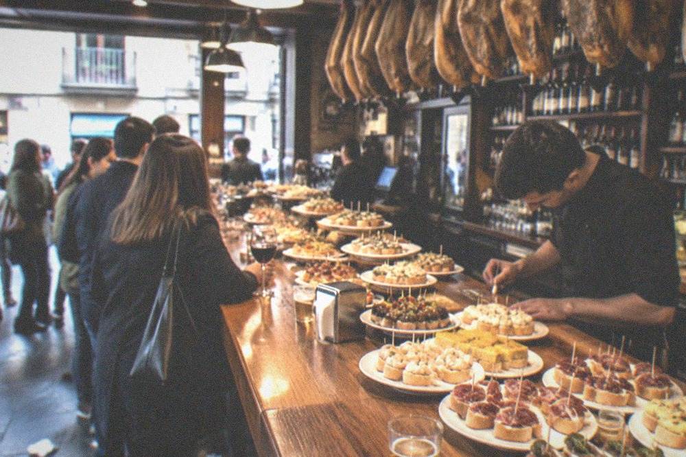 A barman chalking a running order total on the wooden counter of a pintxo bar