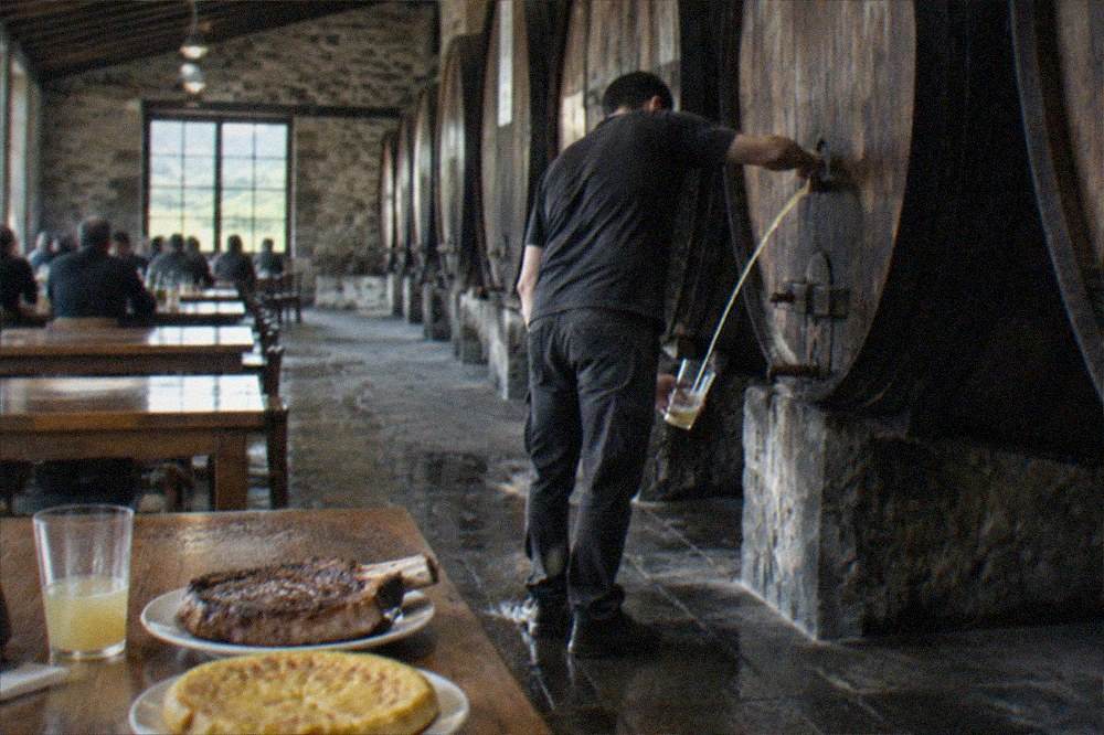 A cider barrel being opened and cider pouring in a long stream into a held glass