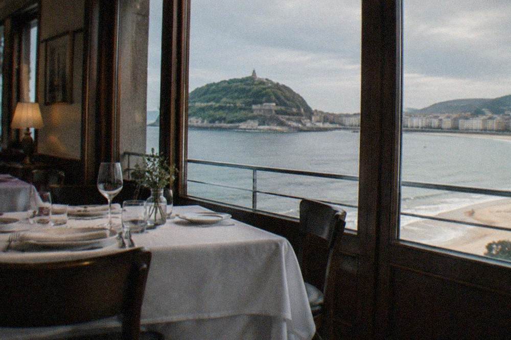 A formal dining room with white tablecloths and a view toward the sea in San Sebastián