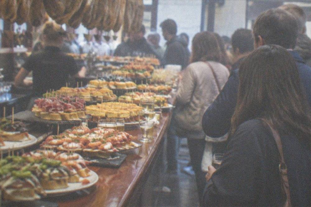 Guests standing at a crowded bar counter with drinks and small plates in San Sebastián
