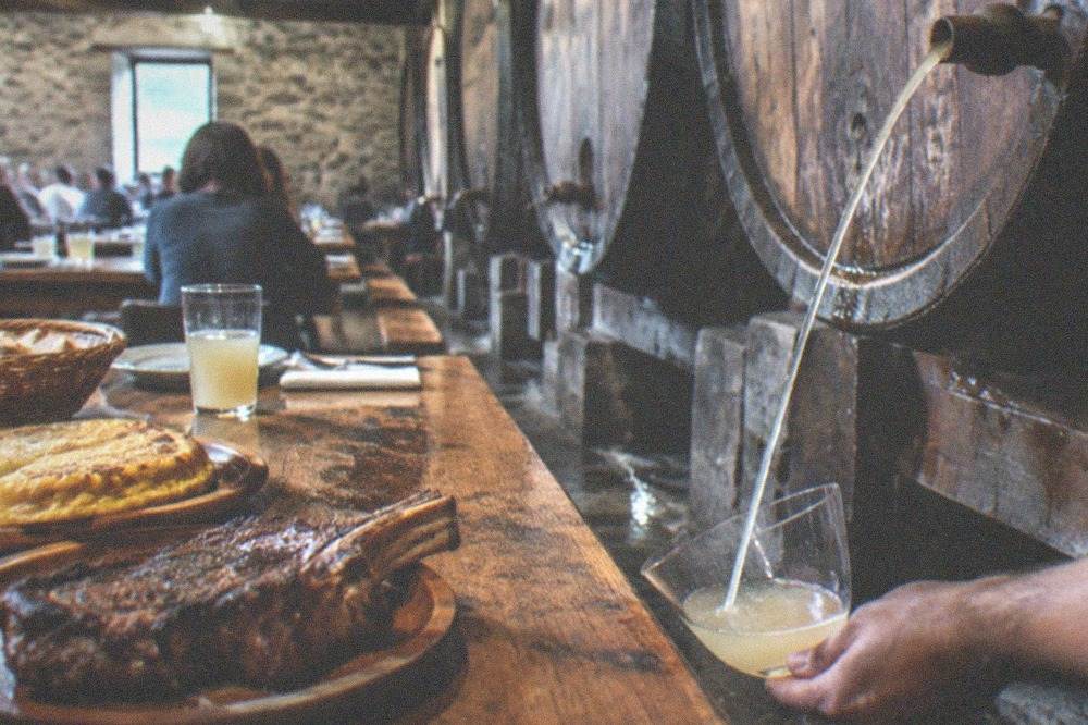 A rustic dining hall with long wooden tables set for a cider house meal near San Sebastián