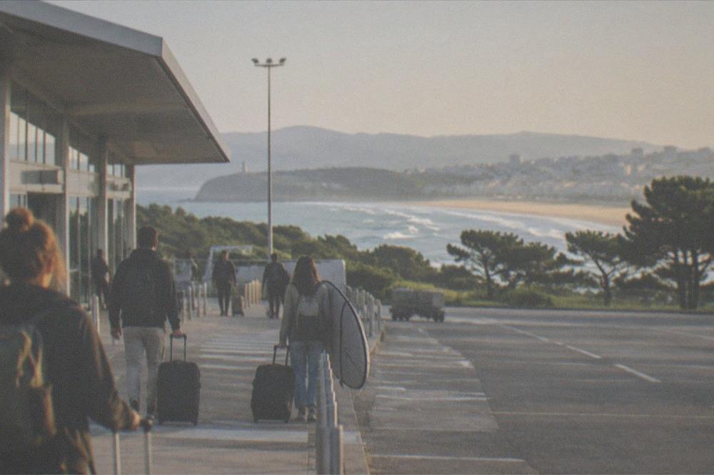 A wide sandy bay curving between a city front and green hills at golden hour