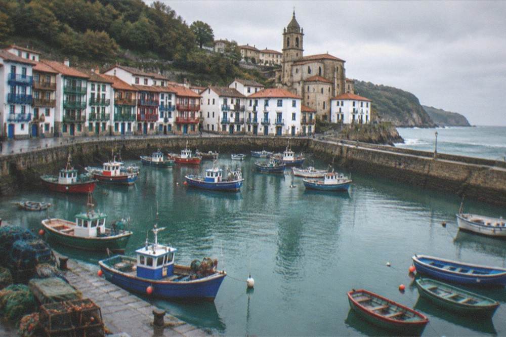 A white coastal town with a church tower above a small harbour of fishing boats