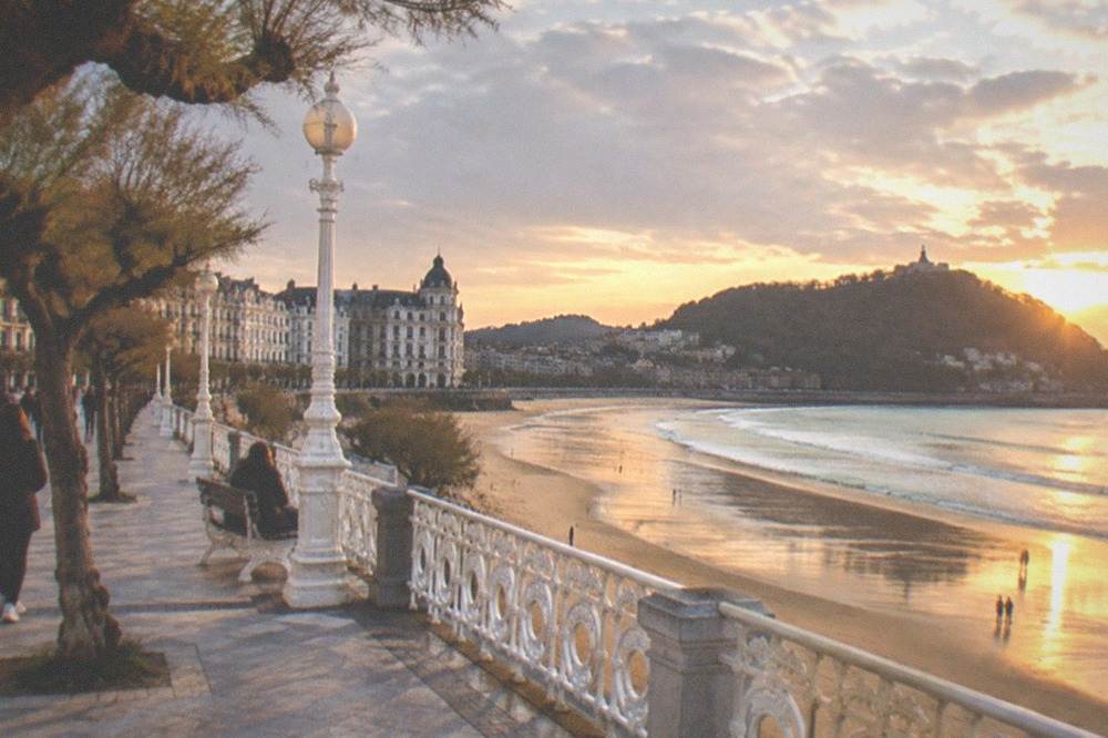 Clouds breaking over La Concha beach with wet sand reflecting the promenade