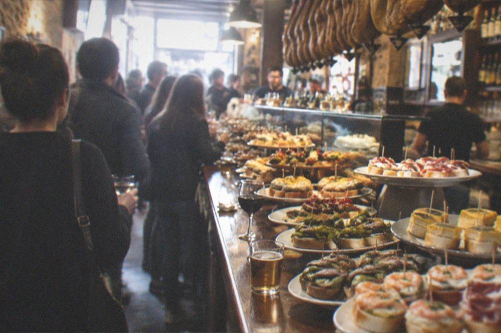 Pintxo bars with crowds standing at the counter in an old town street at night