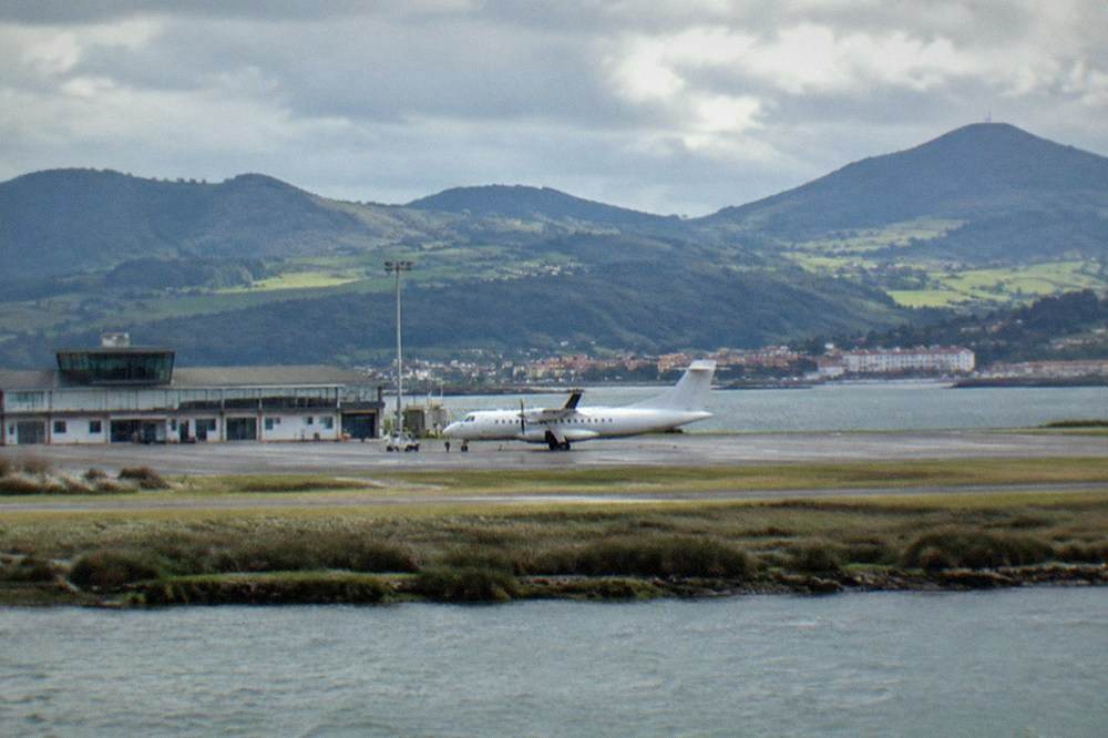 A small regional airport building with hills behind under a cloudy sky