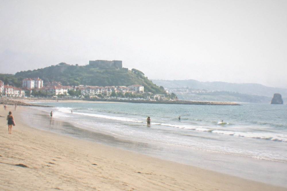 A stone fort on a green hill above a city skyline and a bay