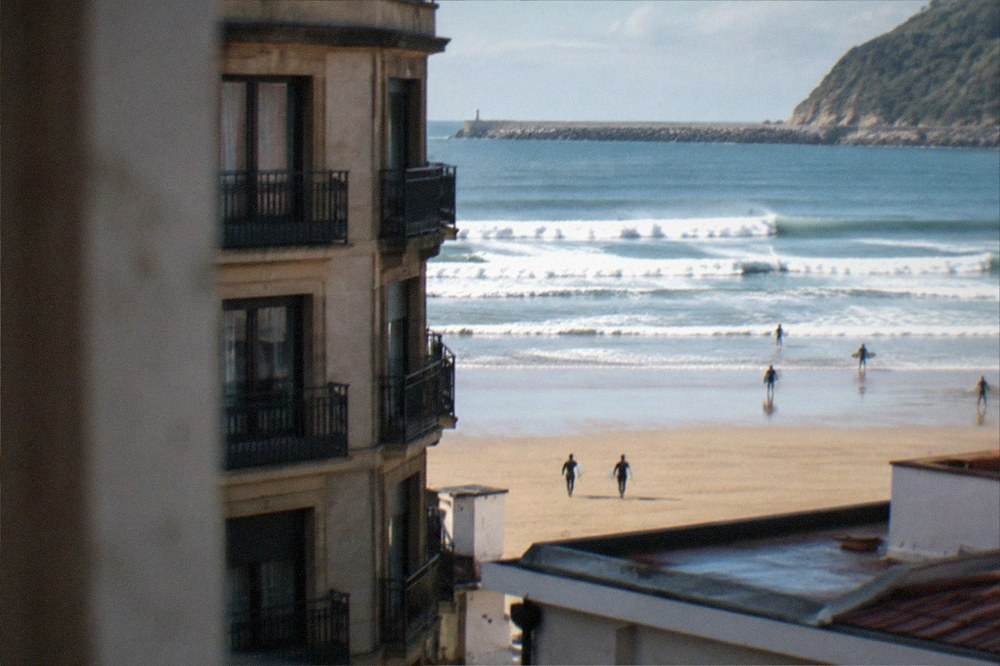 A corner building in the Gros district of San Sebastián with the Zurriola beach and surf visible beyond the rooftops