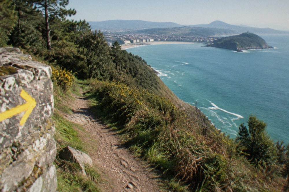 Yellow Camino de Santiago arrow painted on a stone wall beside a coastal path