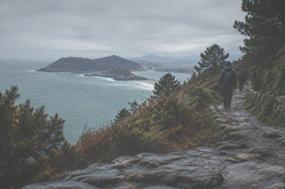 Pilgrims walking at sunrise along a stone coastal track with the sea on the left