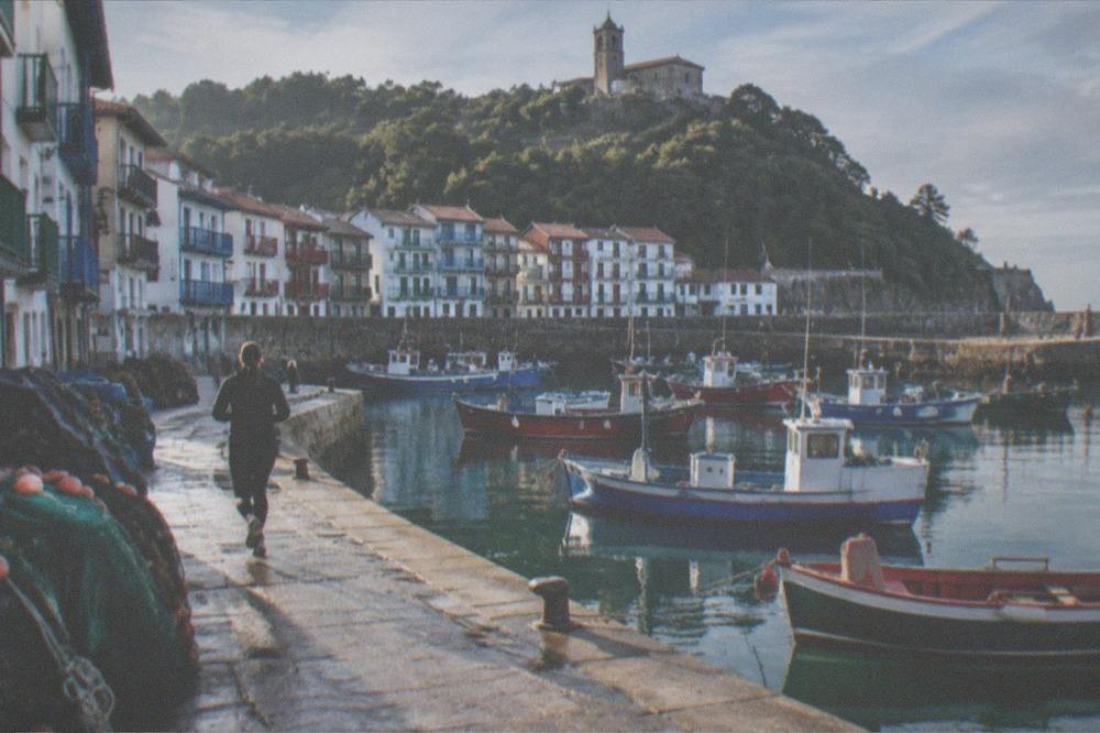 Fishing boats moored in a small Basque harbour with a hilltop church above